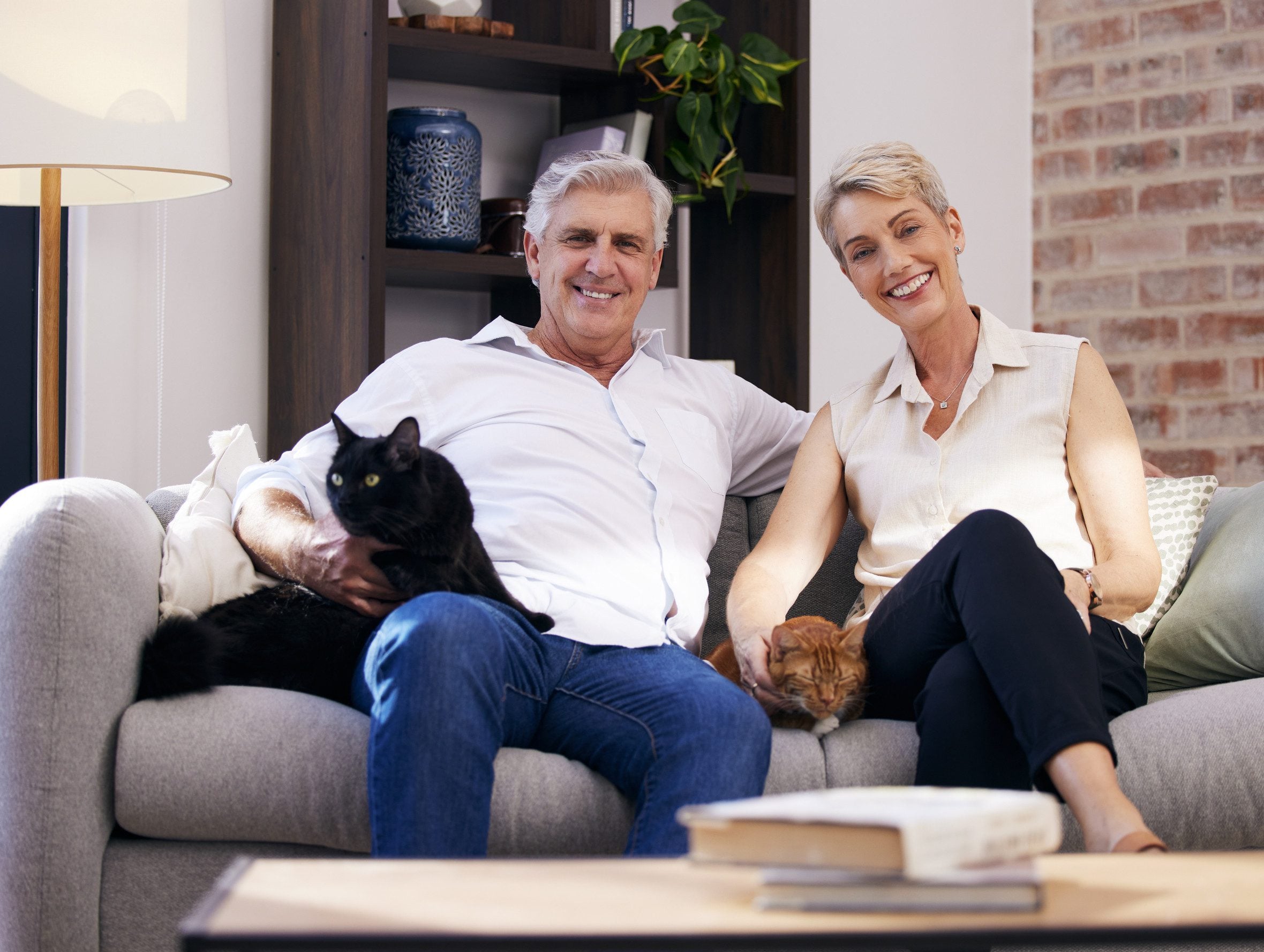 An older couple sitting on their living room sofa with two cats, illustrating how housing rights work under emotional support animal laws in Pennsylvania.