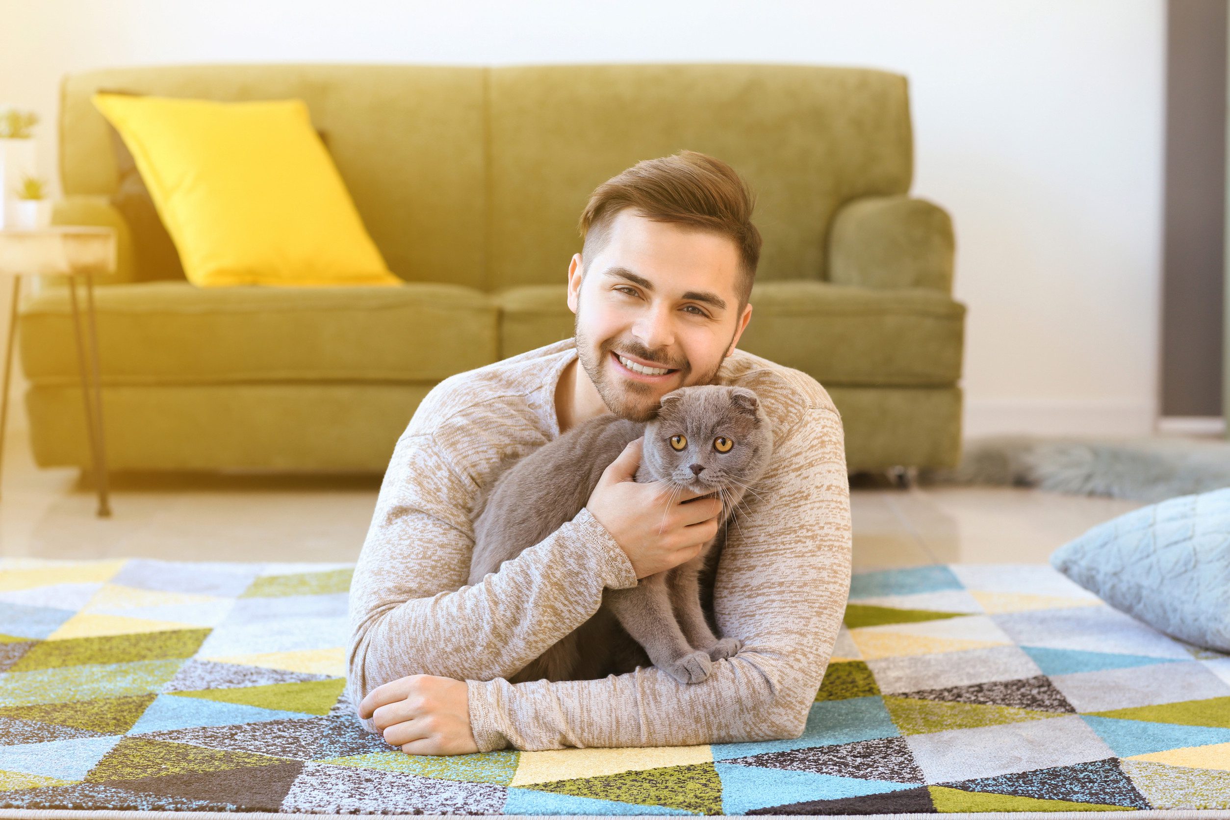A smiling man cuddling his emotional support animal while relaxing on a colorful rug at home in Great Falls, MT.